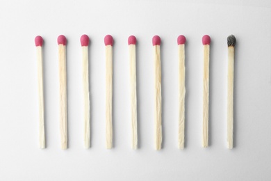 Photo of Row of whole matches and burnt one on white background, top view. Uniqueness concept