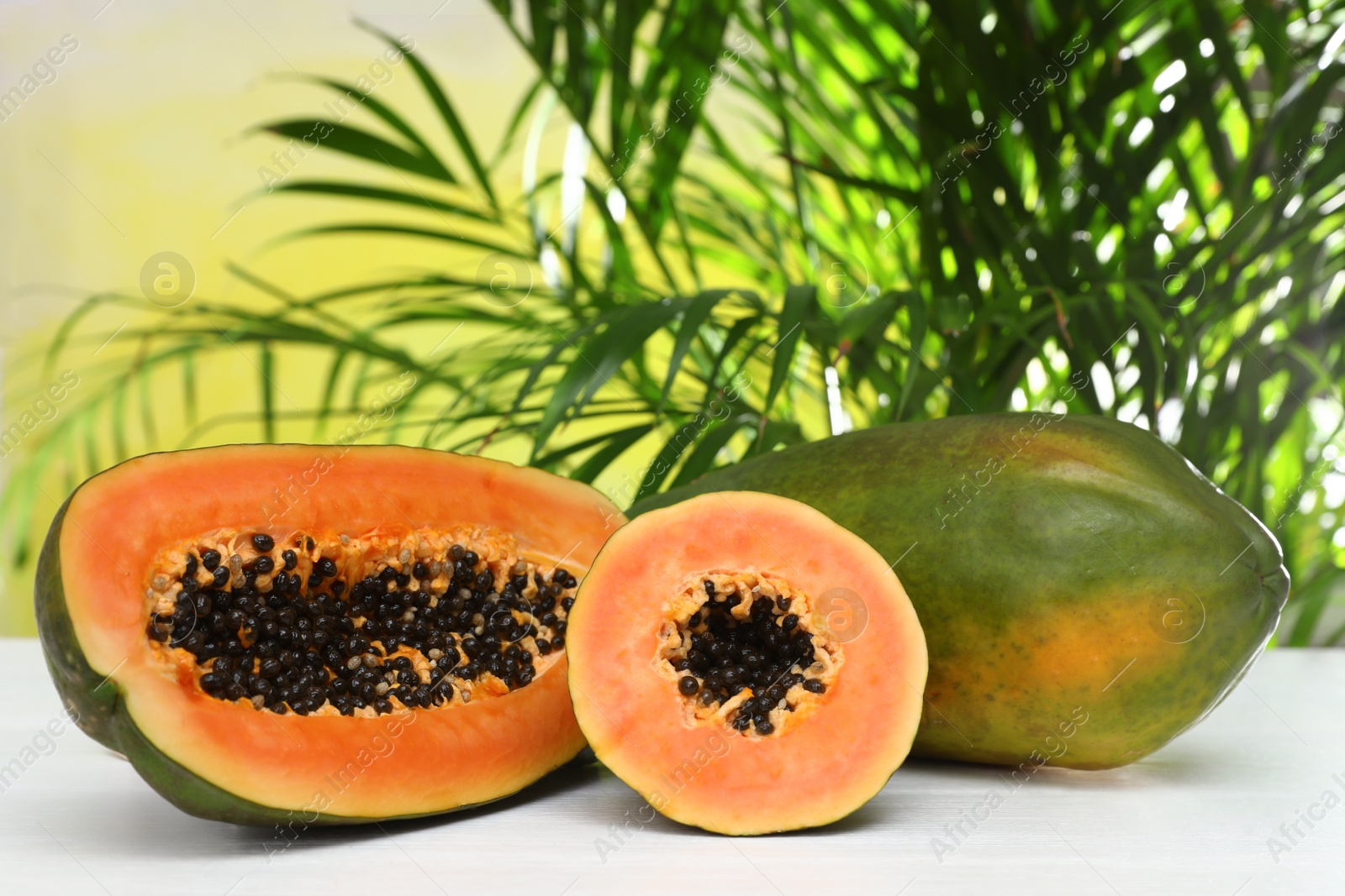 Photo of Fresh juicy papayas on white table against blurred background, space for text