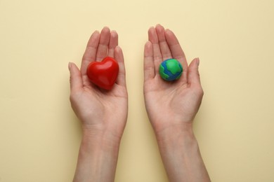 Photo of Woman holding model of planet and red heart on beige background, top view. Earth Day