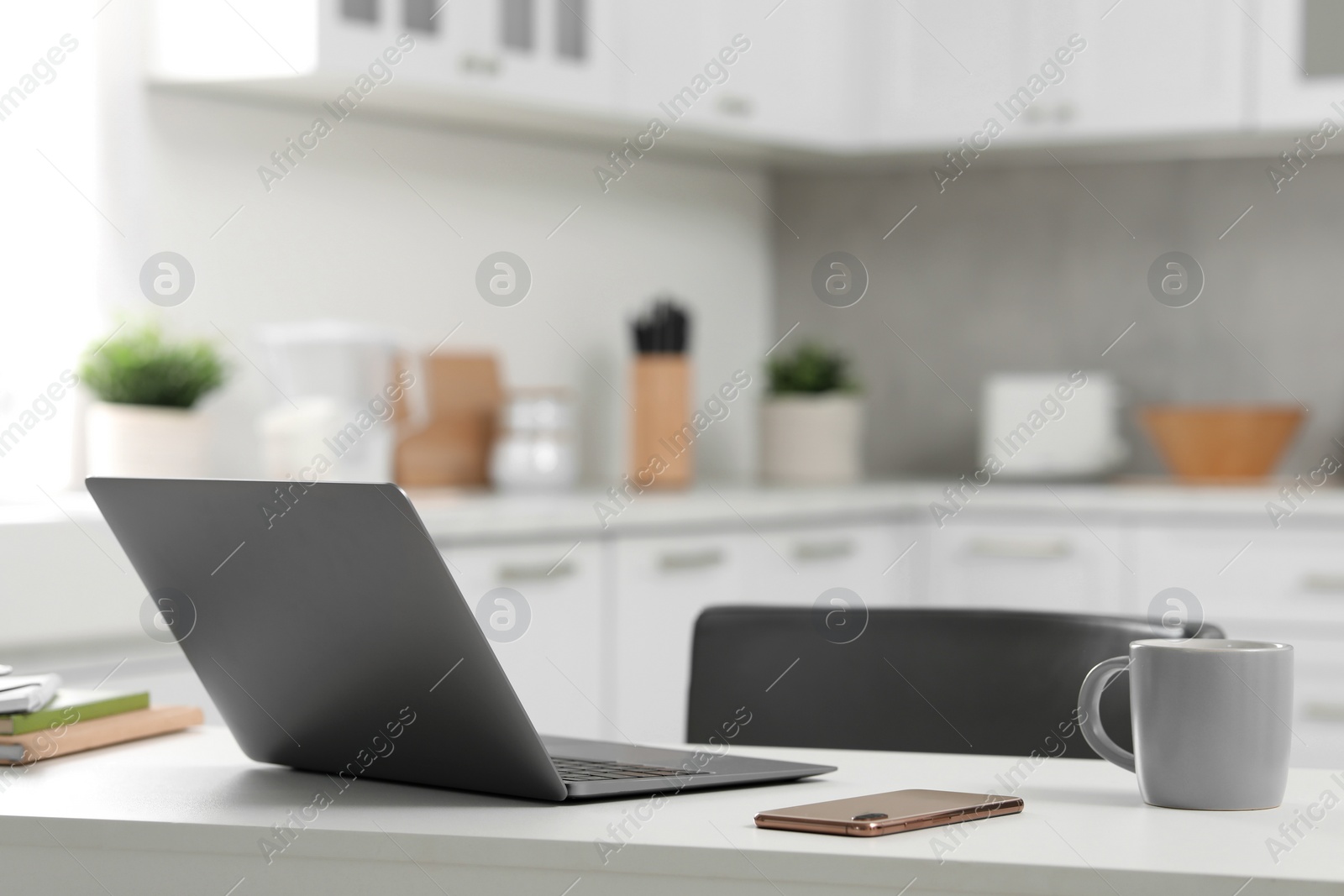 Photo of Home office. Laptop, smartphone and cup on white desk in kitchen, space for text