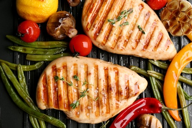 Photo of Tasty grilled chicken fillets with vegetables on frying pan, flat lay