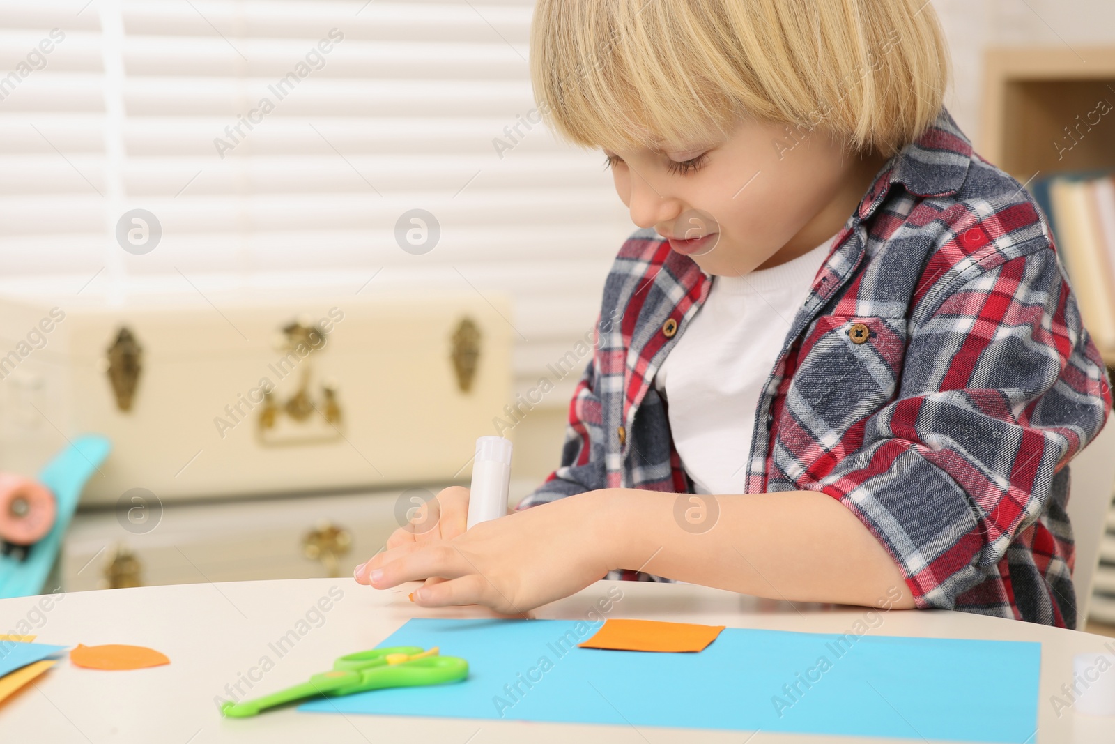 Photo of Boy using glue stick at desk in room, closeup. Home workplace