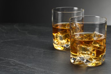 Photo of Whiskey and ice cubes in glasses on grey table, closeup. Space for text