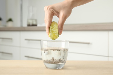 Photo of Young woman squeezing lime into glass of water with chia seeds on table, closeup