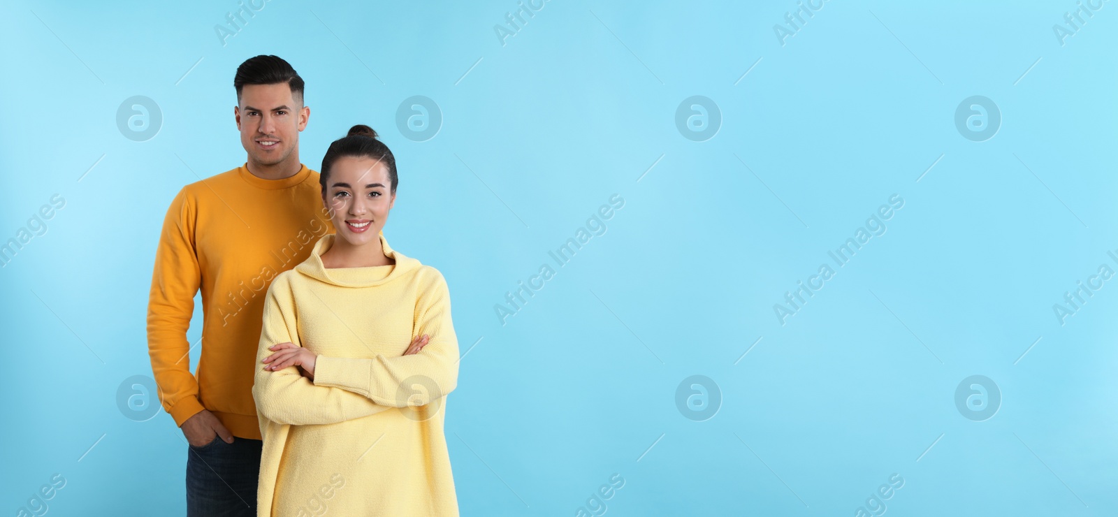 Photo of Happy couple wearing yellow warm sweaters on light blue background. Space for text