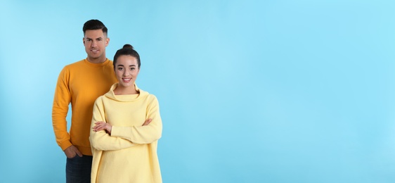 Happy couple wearing yellow warm sweaters on light blue background. Space for text