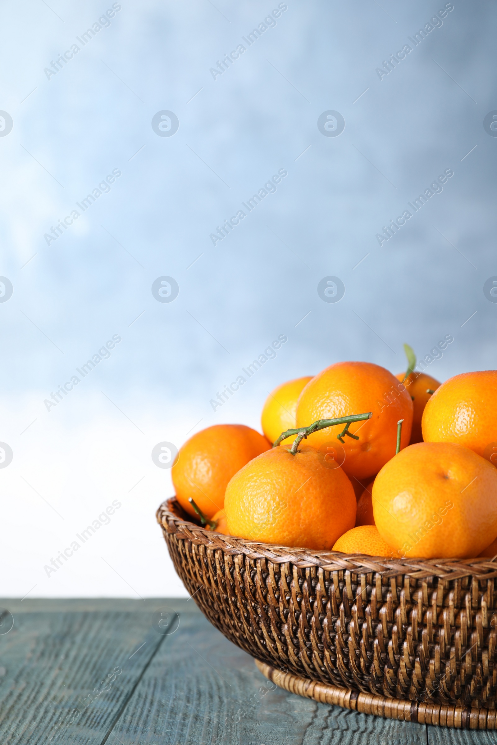Photo of Fresh ripe tangerines on wooden table against light blue background. Space for text