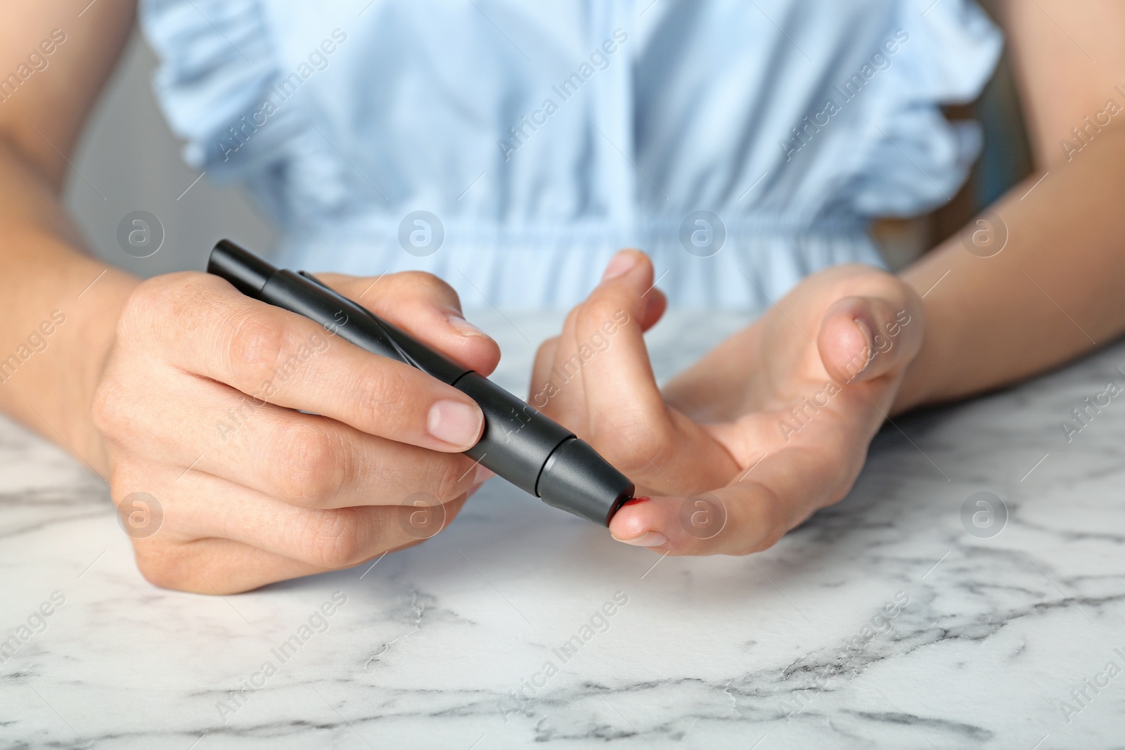 Photo of Woman using lancet pen at table. Diabetes test