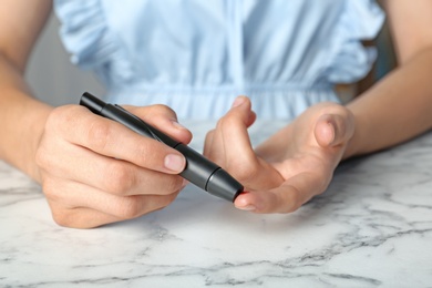 Woman using lancet pen at table. Diabetes test