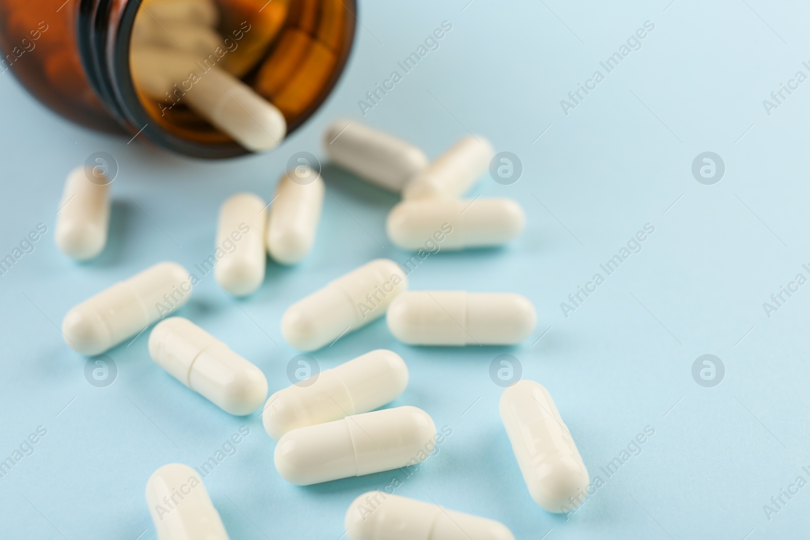 Photo of Bottle and vitamin capsules on light blue background, closeup. Space for text