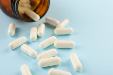 Photo of Bottle and vitamin capsules on light blue background, closeup. Space for text