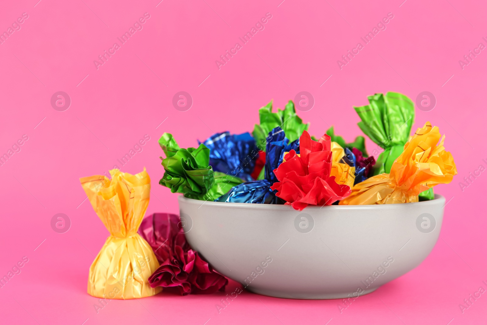 Photo of Candies in colorful wrappers on pink background, closeup