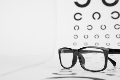 Photo of Vision test chart and glasses on white background, closeup. Space for text