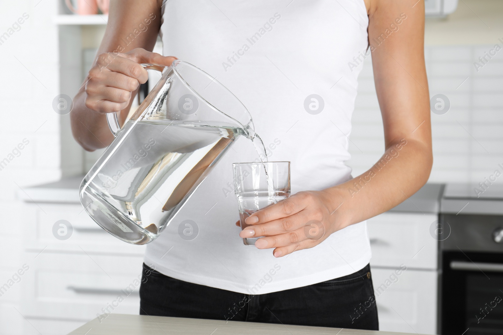 Photo of Woman pouring water into glass at table, closeup