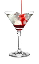 Pouring grenadine into glass of martini cocktail on white background