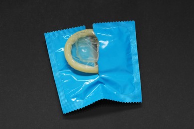 Photo of Condom in torn package on black background, top view. Safe sex