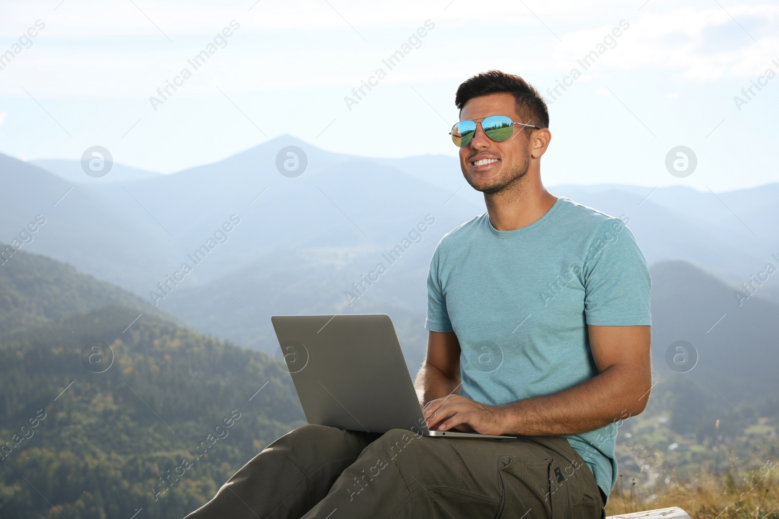 Photo of Man working with laptop in mountains on sunny day