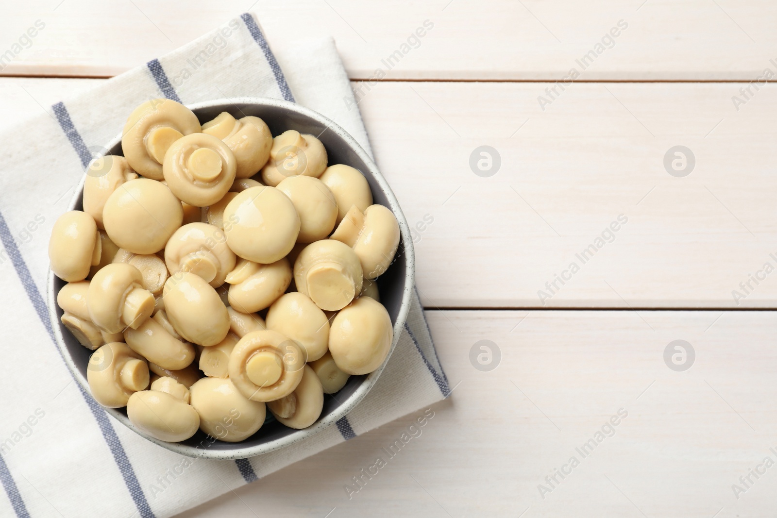 Photo of Delicious marinated mushrooms in bowl on white wooden table, top view. Space for text