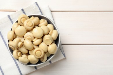 Delicious marinated mushrooms in bowl on white wooden table, top view. Space for text