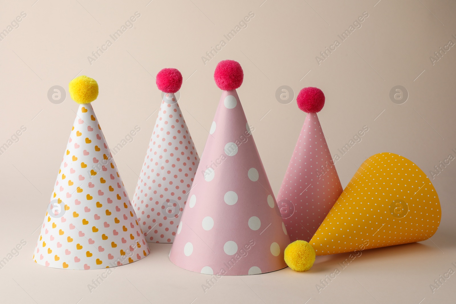Photo of Beautiful party hats with pompoms on beige background