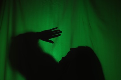 Silhouette of creepy ghost behind dark green cloth