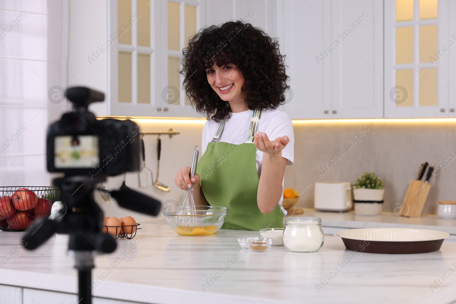 Photo of Smiling food blogger cooking while recording video in kitchen