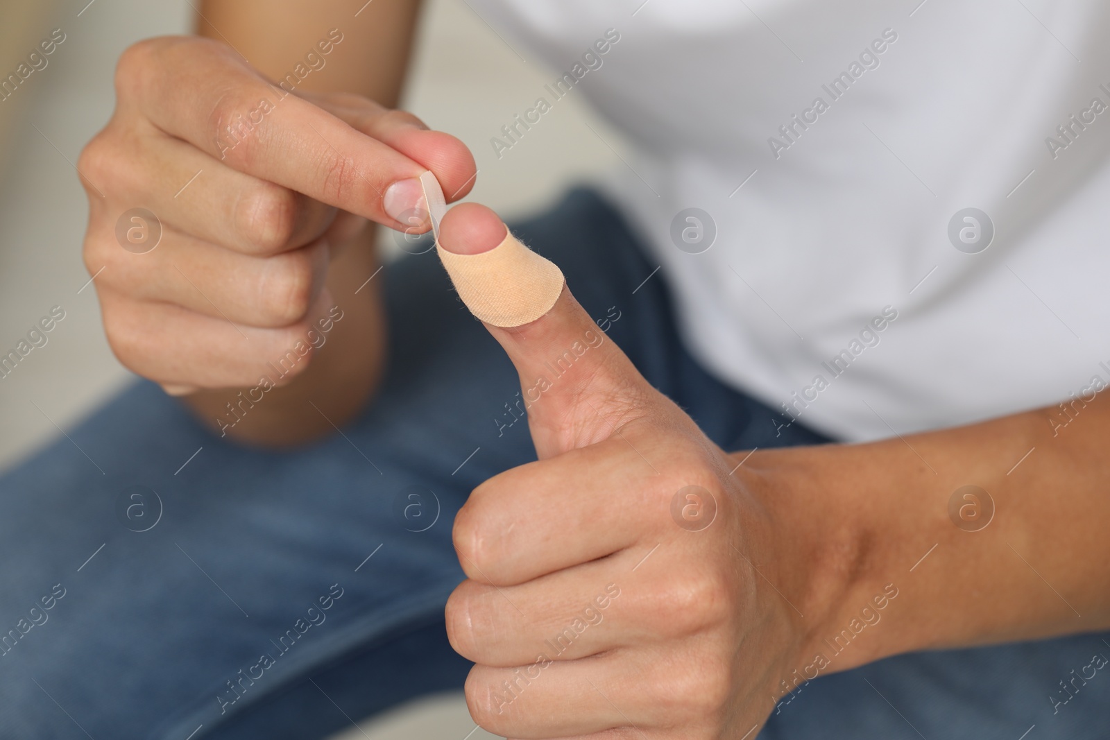 Photo of Man putting sticking plaster onto thumb indoors, closeup