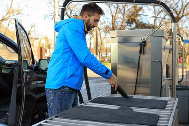 Man cleaning auto carpets with vacuum cleaner at self-service car wash