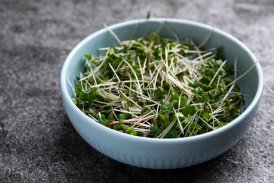 Photo of Bowl with fresh microgreen on grey table, closeup