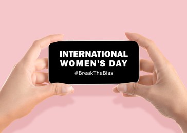 Woman holding smartphone with hashtag BreakTheBias on screen against pink background, closeup. Campaign theme for International Women's Day