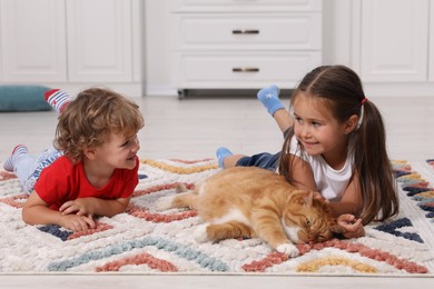 Photo of Little children and cute ginger cat on carpet at home