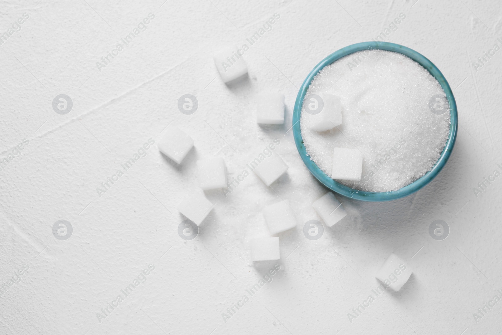 Photo of Different types of sugar in bowl on white table, flat lay. Space for text