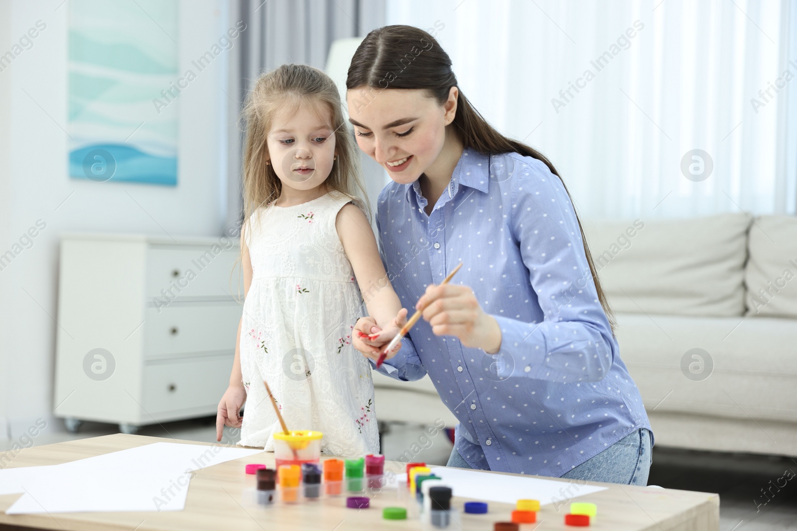 Photo of Mother and her little daughter painting with palms at home