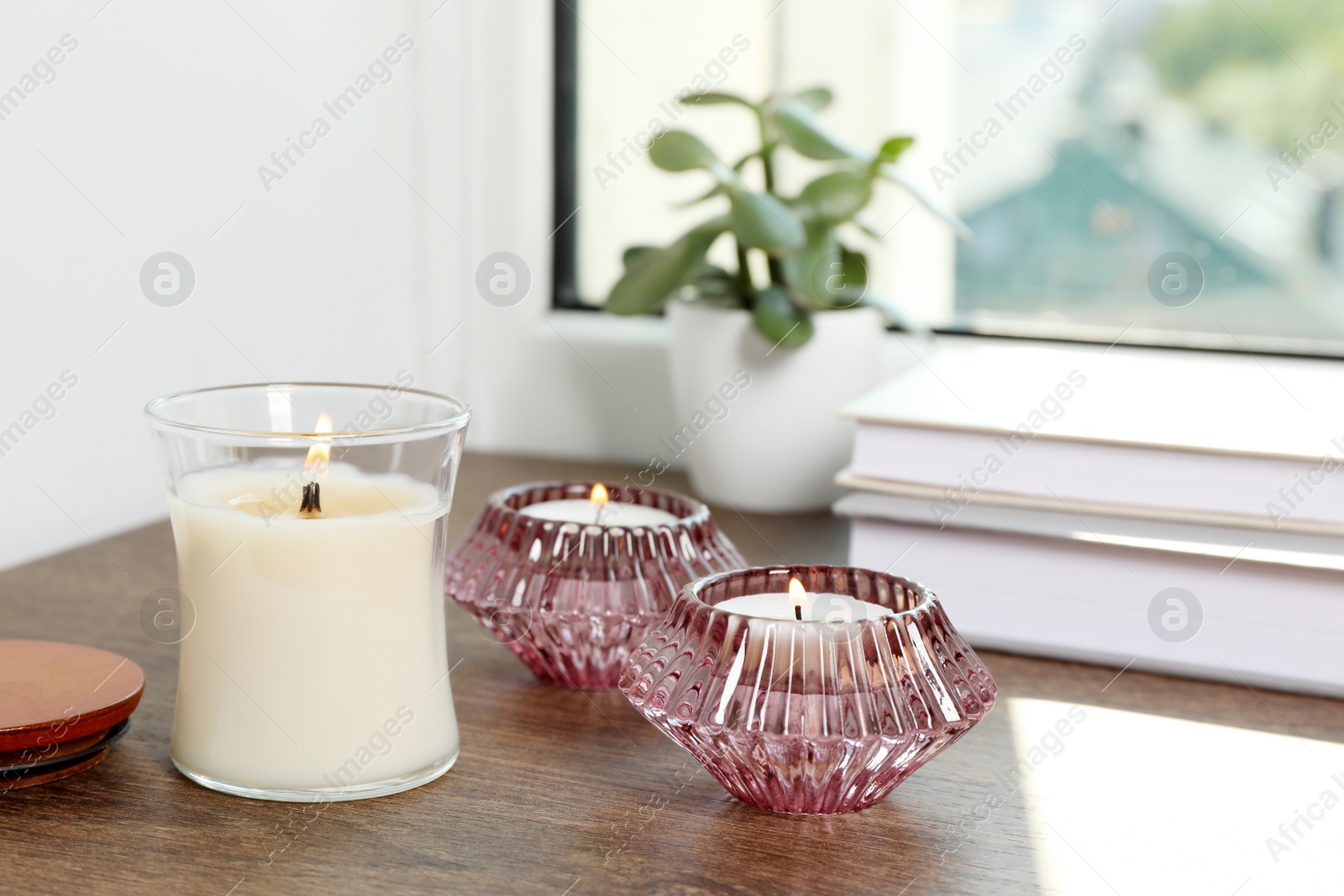 Photo of Burning candles with books and houseplant on wooden window sill