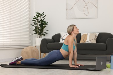 Photo of Online fitness trainer. Woman doing exercise near laptop at home