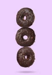 Image of Tasty chocolate donuts falling on pastel violet background