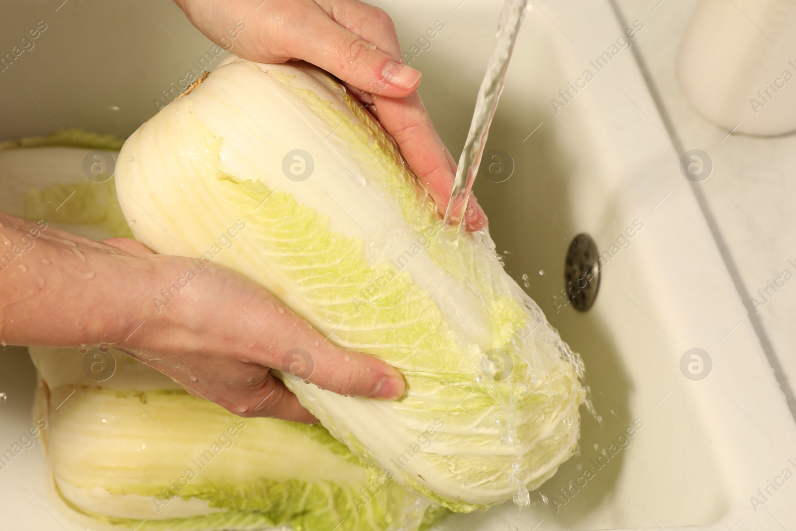 Photo of Woman washing fresh chinese cabbage under tap water in kitchen sink, closeup