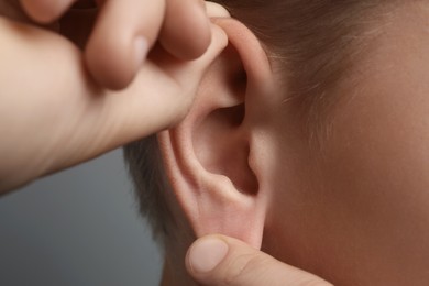 Photo of Boy touching his ear on grey background, closeup