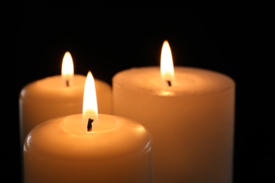 Photo of Wax candles burning on black background, closeup