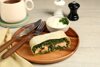 Photo of Piece of delicious strudel with salmon and spinach served on light wooden table
