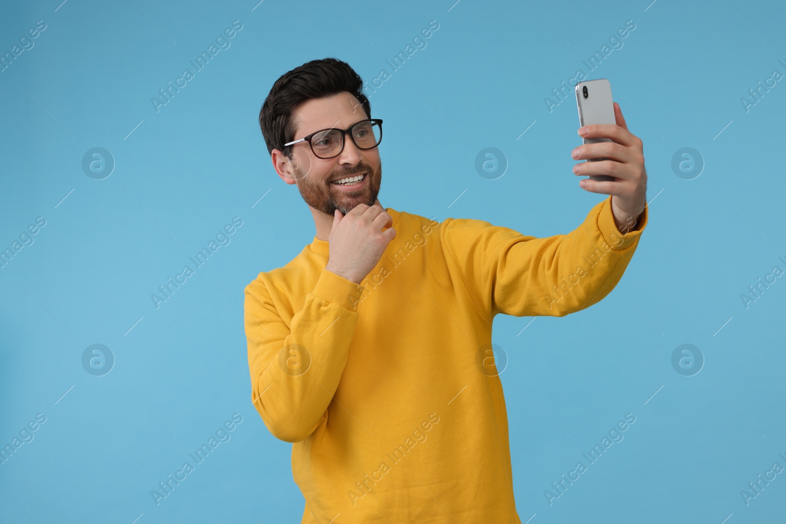 Photo of Smiling man taking selfie with smartphone on light blue background