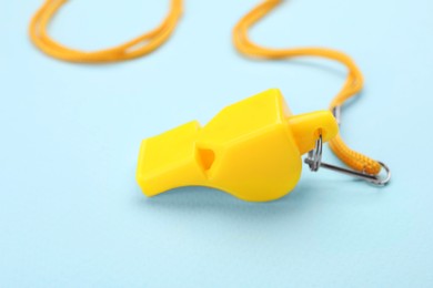 One yellow whistle with cord on light blue background, closeup
