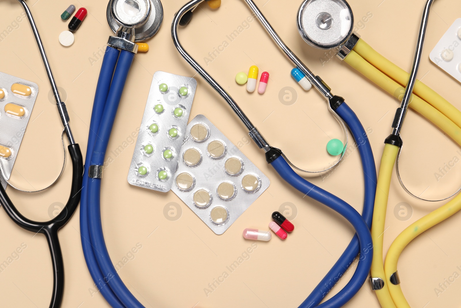 Photo of Stethoscopes and pills on beige background, flat lay. Medical tools