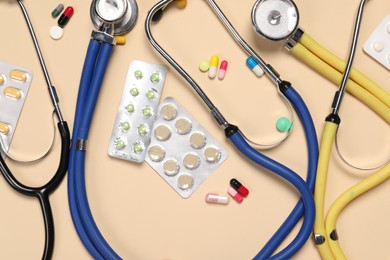 Stethoscopes and pills on beige background, flat lay. Medical tools