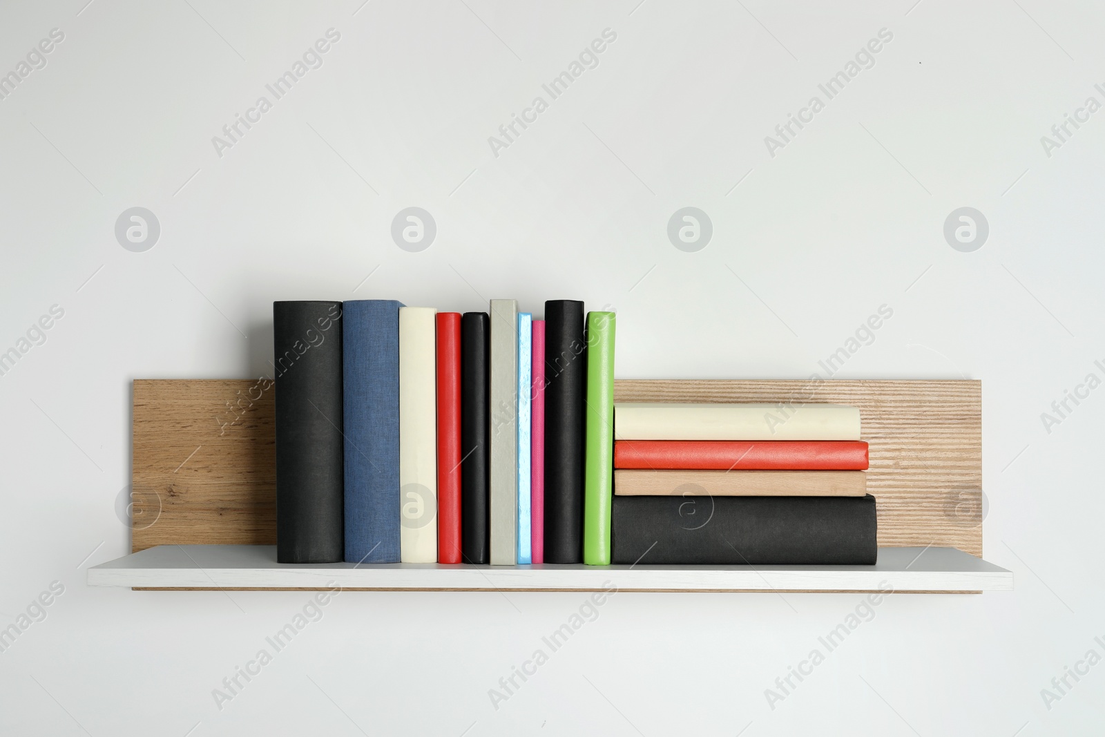 Photo of Different books on wooden shelf near white wall