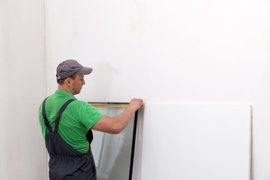 Worker in uniform measuring double glazing window indoors