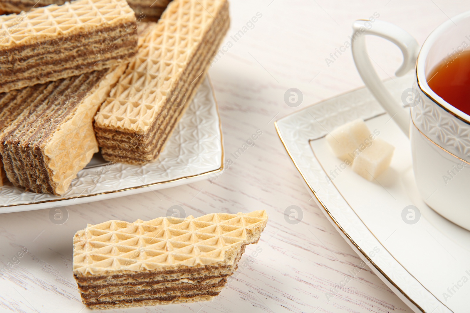 Photo of Plate of delicious wafers with cup of tea on white wooden background, closeup