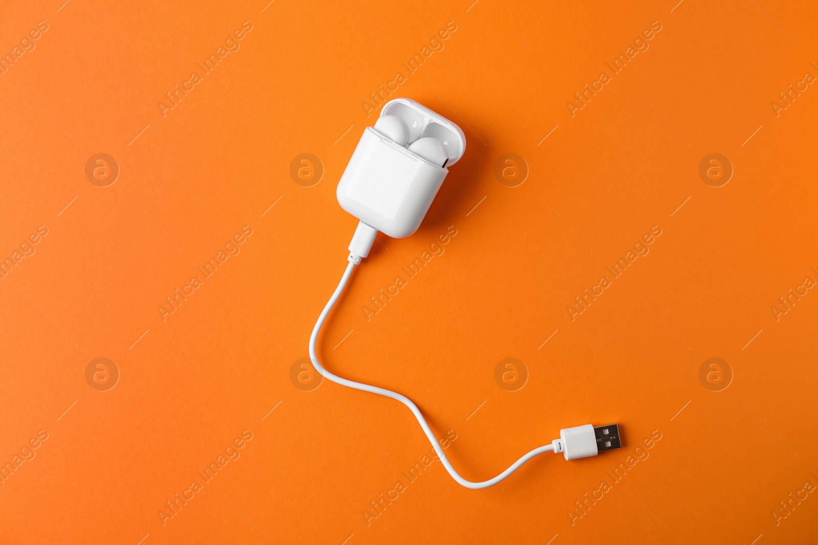 Photo of Modern wireless earphones in charging case with cable on orange background, top view