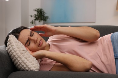 Sad woman suffering from headache on sofa indoors