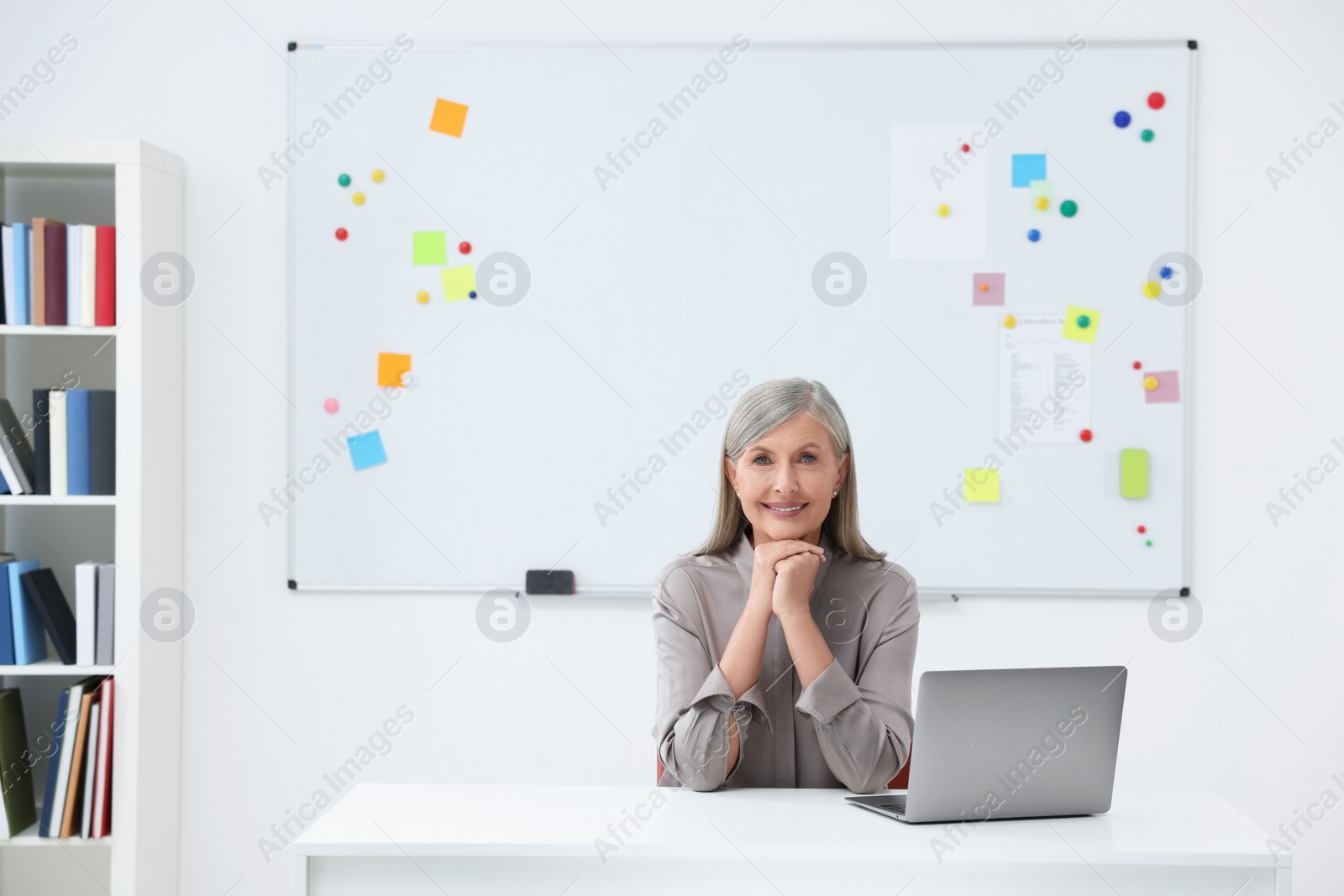 Photo of Professor sitting near laptop at desk in classroom, space for text